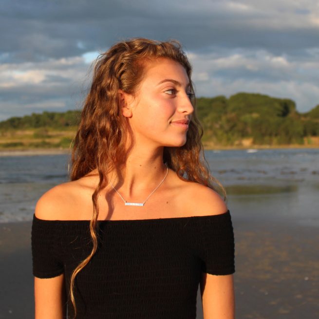 girl on a maine beach wearing an ohm mani padme hum necklace by veda